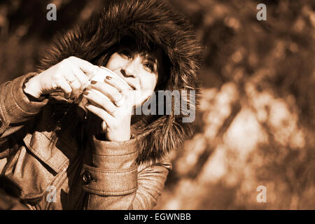 Frau in Kapuzenjacke heiß dampfenden Kaffee in sepia Stockfoto