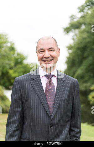 eine professionelle Geschäftsmann / Hotelmanager steht in den Gärten von einer englischen Landhaushotel in einem Business-Anzug Stockfoto