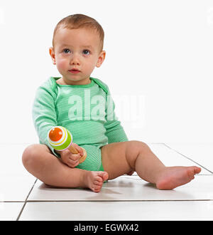 Baby Junge (12,5 Monate) sitzt mit einer Rassel spielen Stockfoto