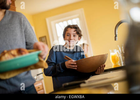 Eine Frau, die zubereiteten Speisen auf den Tisch. Ein Junge mit einem großen Holzschale. Stockfoto