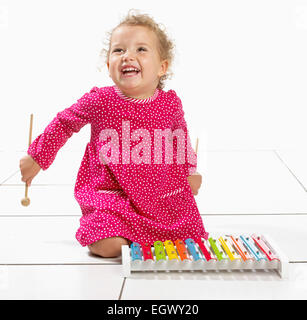 Kleines Mädchen (2 Jahre) kniend am Boden neben Xylophon Stockfoto