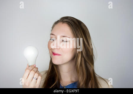 Hübsche Geschäftsfrau blaues Top und gelbe Jacke hält eine Glühbirne Stockfoto