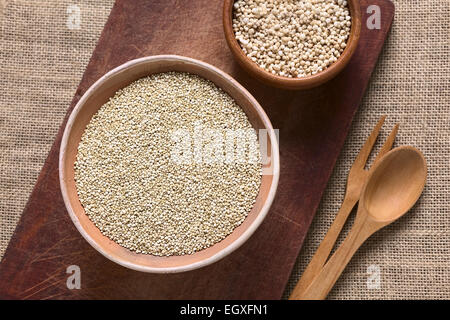 Obenliegende Aufnahme von rohen weißen Quinoa (Chenopodium Quinoa lat.) Getreide Samen in Schüssel mit geplatzten Quinoa Getreide auf Holzbrett Stockfoto