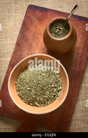 Südamerikanischen Yerba Mate (Mate-Tee) getrocknete Blätter in Ton Schüssel mit einer hölzernen Mate Tasse mit Tee gefüllt Stockfoto