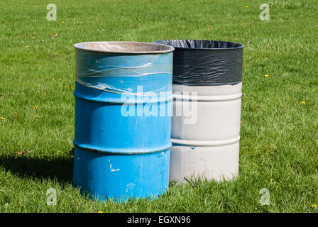 Zwei große blaue und graue Mülltonnen auf dem grünen Rasen mit Mülltüten im Inneren. Stockfoto