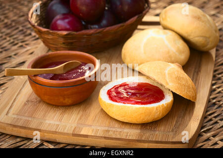 Pflaumenmus verteilt auf Brötchen mit Pflaumen im Korb auf Holzbrett fotografiert mit natürlichem Licht (Tiefenschärfe) Stockfoto