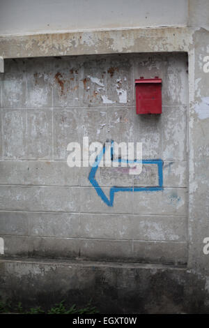 Äußere Brise Blockwand in einem schlechten Zustand mit einem roten Briefkasten und blauen Punkt links Pfeil, Talat Phlu, Bangkok, Thailand. Stockfoto