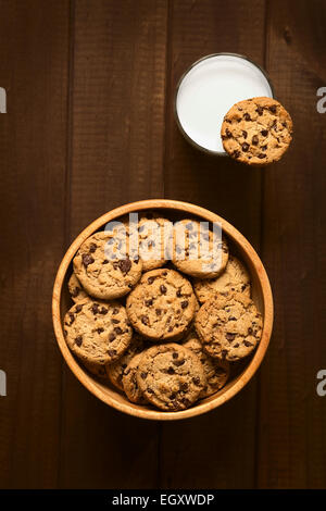 Chocolate Chip Cookies in Holzschale und ein Cookie auf der Felge ein Glas kalte Milch mit Tageslicht fotografiert Stockfoto