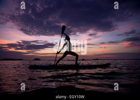 Eine junge Frau erstreckt sich auf einem Surfbrett während einer Yoga-Lektion Stockfoto