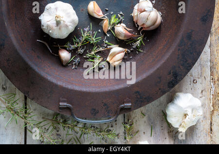 Knoblauch mit Rosmarin in einen alten rostigen Topf platziert auf einem weißen Bauernhaus Küche Holztisch, mit Platz für text Stockfoto