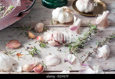 Knoblauch mit Rosmarin in einen alten rostigen Topf platziert auf einem weißen Bauernhaus Holztisch mit Platz für text Stockfoto