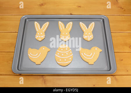 Osterkekse dekoriert mit weißem Zuckerguss auf einem Backblech auf einem Holztisch Stockfoto