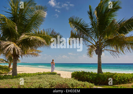 Frau (Kaukasier), zurück zur Kamera, umrahmt von Kokosnuss-Palmen, Blick auf ein Türkis Meer und Sandstrand Strand. Stockfoto