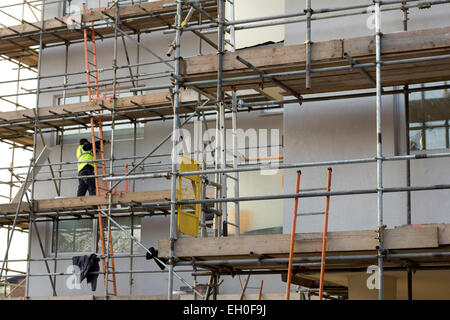 Mann arbeiten auf Gerüsten am Wohnblock. Bauarbeiten, Rendering und Modernisierung der Außenwände der Wohnungen. Stockfoto