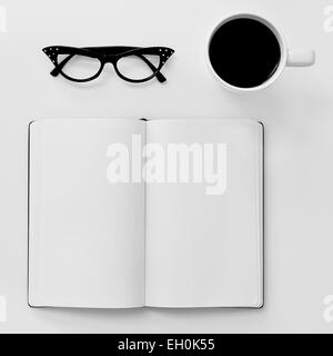 High-Angle Shot eine leere Arbeitsmappe, ein paar schwarze Kunststoff-umrandeten Brille für Frauen und eine Tasse Kaffee auf einem weißen Tisch Stockfoto