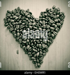 ein Haufen von gerösteten Kaffeebohnen bilden eine Herz auf einem Holztisch, in schwarz und weiß Stockfoto