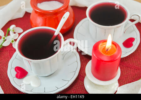 Zwei Tassen Hibiskustee dekoriert mit zwei Herzen und eine brennende Kerze Stockfoto