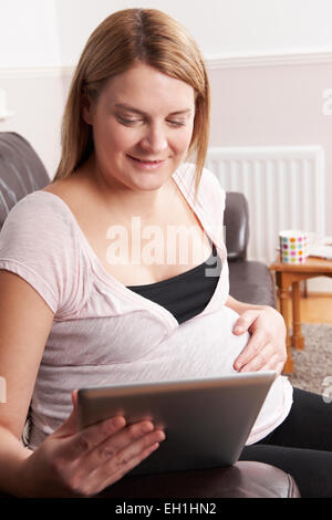 Schwangere Frau, die mit digitalen Tablet zu Hause entspannend Stockfoto