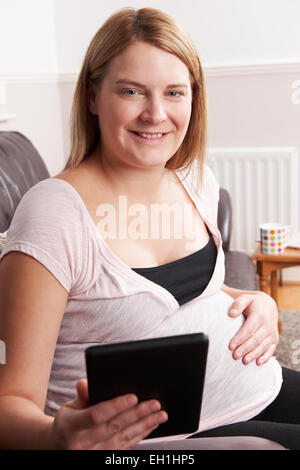 Schwangere Frau, die mit E-Reader zu Hause entspannen Stockfoto
