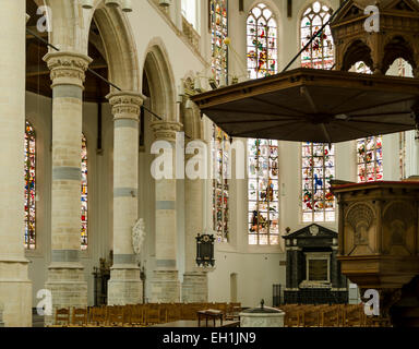 Innere des "Oude Kerk" von Delft mit großen Säulen, Glasmalerei, eine Kanzel und Holzstühlen. Stockfoto