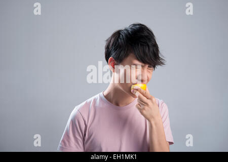 Junger Mann isst Zitrone Stockfoto