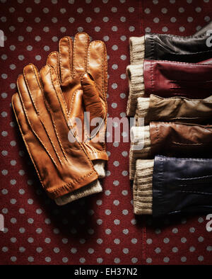 Handschuhe aus Leder in verschiedenen Farben auf gepunkteten roten Stoff, Studioaufnahme Stockfoto