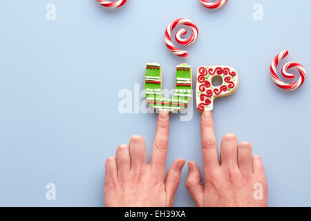 Obenliegende Ansicht des Weibes Hände und Weihnachtsgebäck Zucker Rechtschreibung auf blauem Hintergrund mit Candy Cane wirbelt Stockfoto