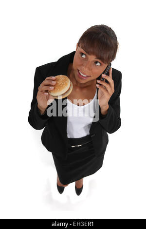 Geschäftsfrau einen Hamburger Essen und sprechen über ihre Zelle Stockfoto