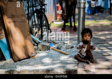 Eine kleine Obdachlosen Straßenkind sitzt am Straßenrand der Kamera mit der Hand heraus suchen. Stockfoto