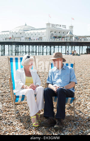 ein Ehepaar mittleren Alters sitzen auf den Liegestühlen, entspannen und genießen ihren Ruhestand, am Strand von Brighton, Stockfoto