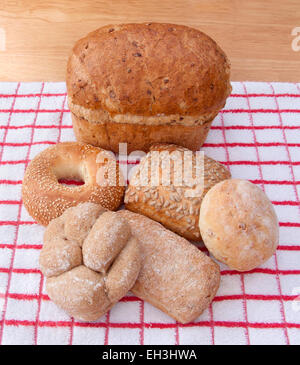 Kornkammer Laib und verschiedenen Brötchen auf einem roten und weißen Tuch mit einem blassen Holz Hintergrund. Stockfoto