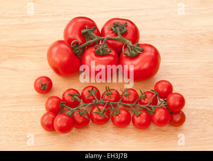 Großen Fleischtomaten mit kleiner Piccolo Kirschtomaten am Rebstock auf einem blassen Holz Hintergrund. Stockfoto