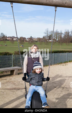 Mutter drängt Kleinkind auf einer Schaukel auf einem Spielplatz Stockfoto