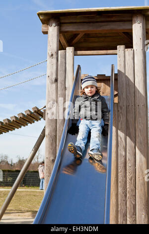 3 Jahre alter Junge auf einer Folie auf Spielplatz in Surrey herab. Stockfoto