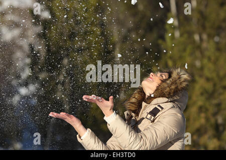 Glückliches Mädchen werfen Schnee in der Luft im Winter Feiertage in einem Wald, an einem sonnigen Tag Stockfoto