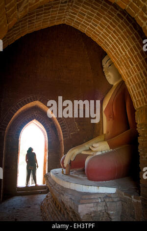 Eine Frau schaut auf auf Buddha-Statue in einem Tempel in Bagan, Myanmar Stockfoto