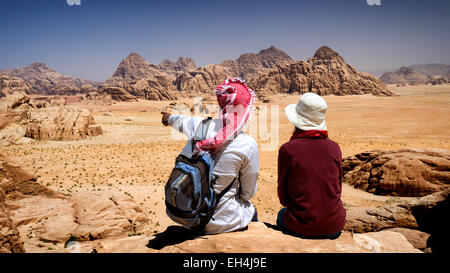 Jordan, Wüste Wadi Rum, geschützten Bereich Weltkulturerbe von UNESCO, Touristen und lokalen Beduinen als Führer auf einem Felsen sitzend betrachten die Landschaft aus der Berg Jebel Burdah Stockfoto