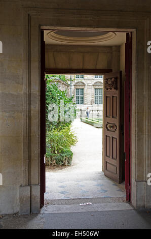 Eine geschnitzte Holztüre öffnet aus dem Arcade-von der Place des Voges in den Garten des Hôtel Sully, Paris. Stockfoto