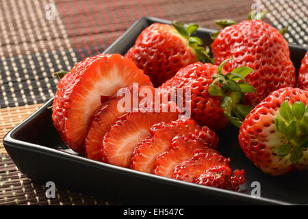 Einzelne wohlgeformte Erdbeere mit Blätter in Gruppe von Erdbeeren. Stockfoto
