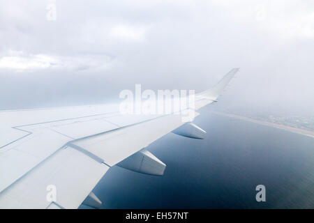 Blick aus dem Flugzeug, dem Flügel des Flugzeugs und das Land aus dem Fenster an einem nebeligen nebligen Tag sichtbar. Stockfoto