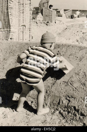 Deutschland. 28. Februar 2015. CA. 1960er Jahre: Kleiner Junge in einem gestreiften T-shirt und Shorts am Strand bauen eine Burg aus Sand, mit einem professionellen Bau Werkzeuge © Igor Golovniov/ZUMA Draht/Alamy Live News Stockfoto