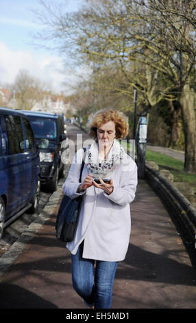 Reife Frau, die mit ihrem Mobiltelefon die Straße entlang läuft Stockfoto
