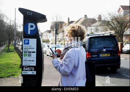 Weibliche Fahrer zahlt für die Parkuhr mit einem Paybyphone Handy-app in Brighton UK Stockfoto