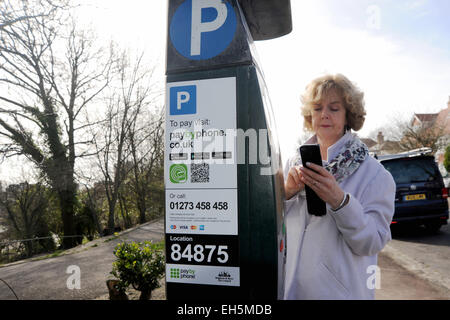 Weibliche Fahrer zahlt für die Parkuhr mit einem Paybyphone Handy-app in Brighton UK Stockfoto