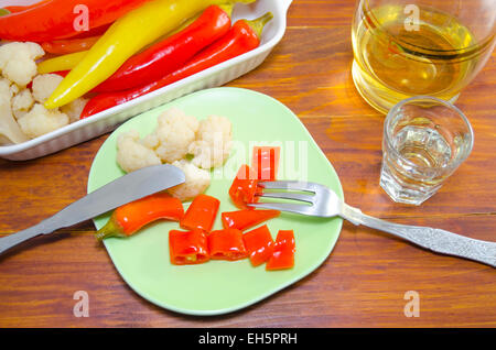 Eingelegte Paprika, Blumenkohl und Oliven auf einer Platte mit einem Messer und eine Gabel und einen Schuss Brandy Stockfoto