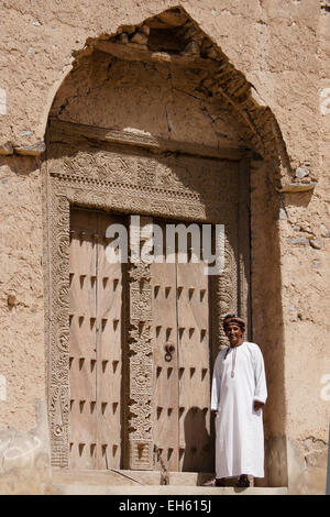 Mann in geschnitzte Holz Tür des alten Lehmziegeln bauen, Al-Mudayrib, Oman Stockfoto