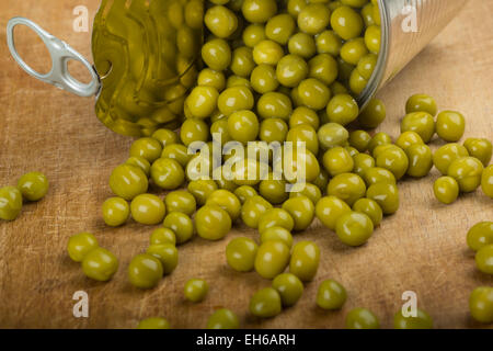 Grüne Erbsen aus einer Blechdose übergreifen Holz Hintergrund Stockfoto