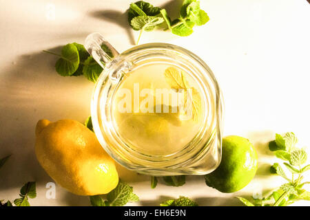 A kann voll von Tee auf einem weißen Tisch, in der Nähe von Zitrone, Limette und Minze Stockfoto