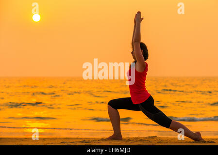 Frau engagiert im Yoga bei Sonnenuntergang am Meer Stockfoto