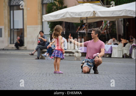 Ein Vater kniete auf der Straße und nimmt eine Selfie von sich selbst, während die kleine Tochter ist gerade, Rom, Italien. Stockfoto